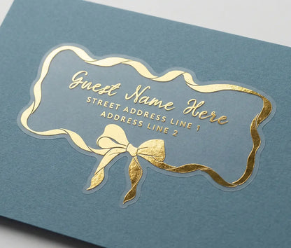 Guest address label printed in gold foil applied to a blue colour envelope with custom die-cut whimsical bow and ribbon shape.