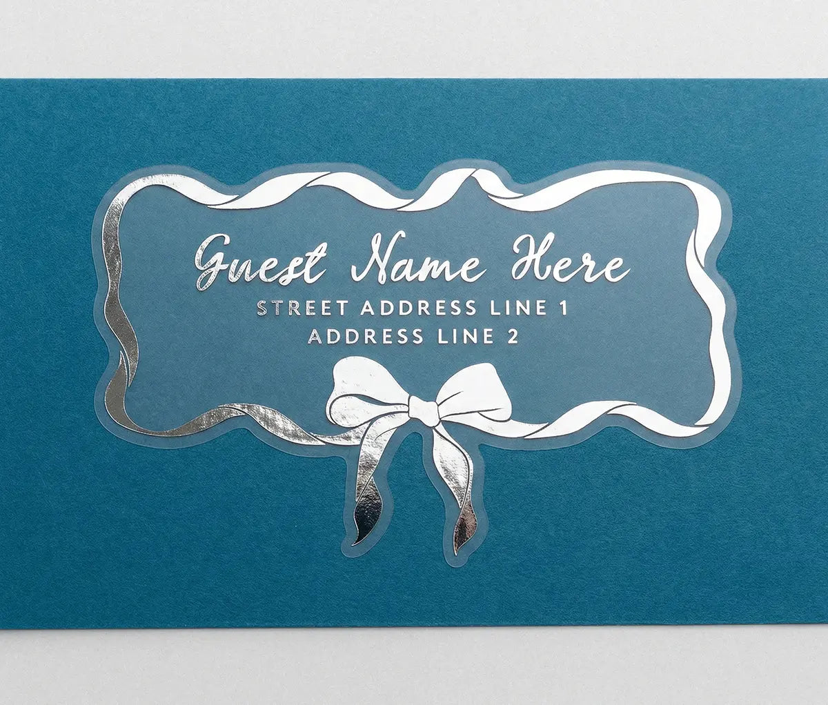 Personalized recipient address label with silver print ribbon and bow design on a blue envelope.