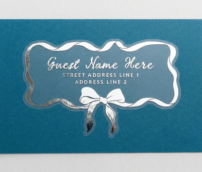Personalized recipient address label with silver print ribbon and bow design on a blue envelope.