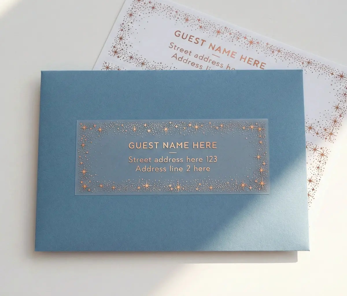 Guest address label with starry frame printed in rose gold foil applied to a slate blue envelope.