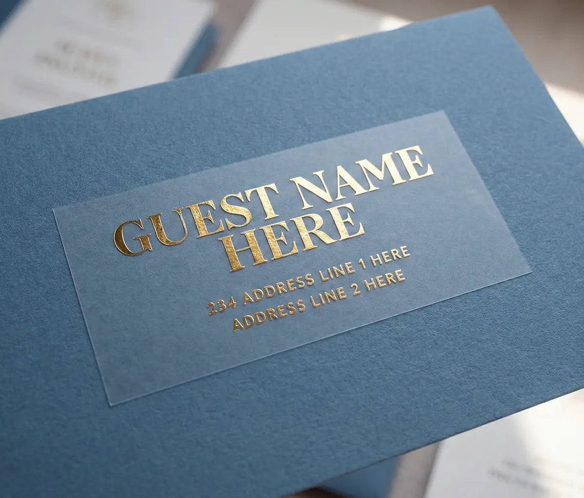 Custom Guest address sticker featuring bold typography printed in gold foil on transparent matte vinyl and applied to a blue envelope.