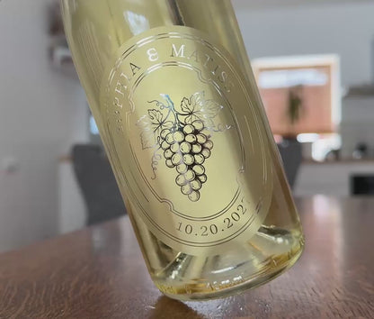 Personalized frosted wedding favour sticker applied to a white wine bottle. Bottle is being rotted slightly to show the shine of the silver foil print.
