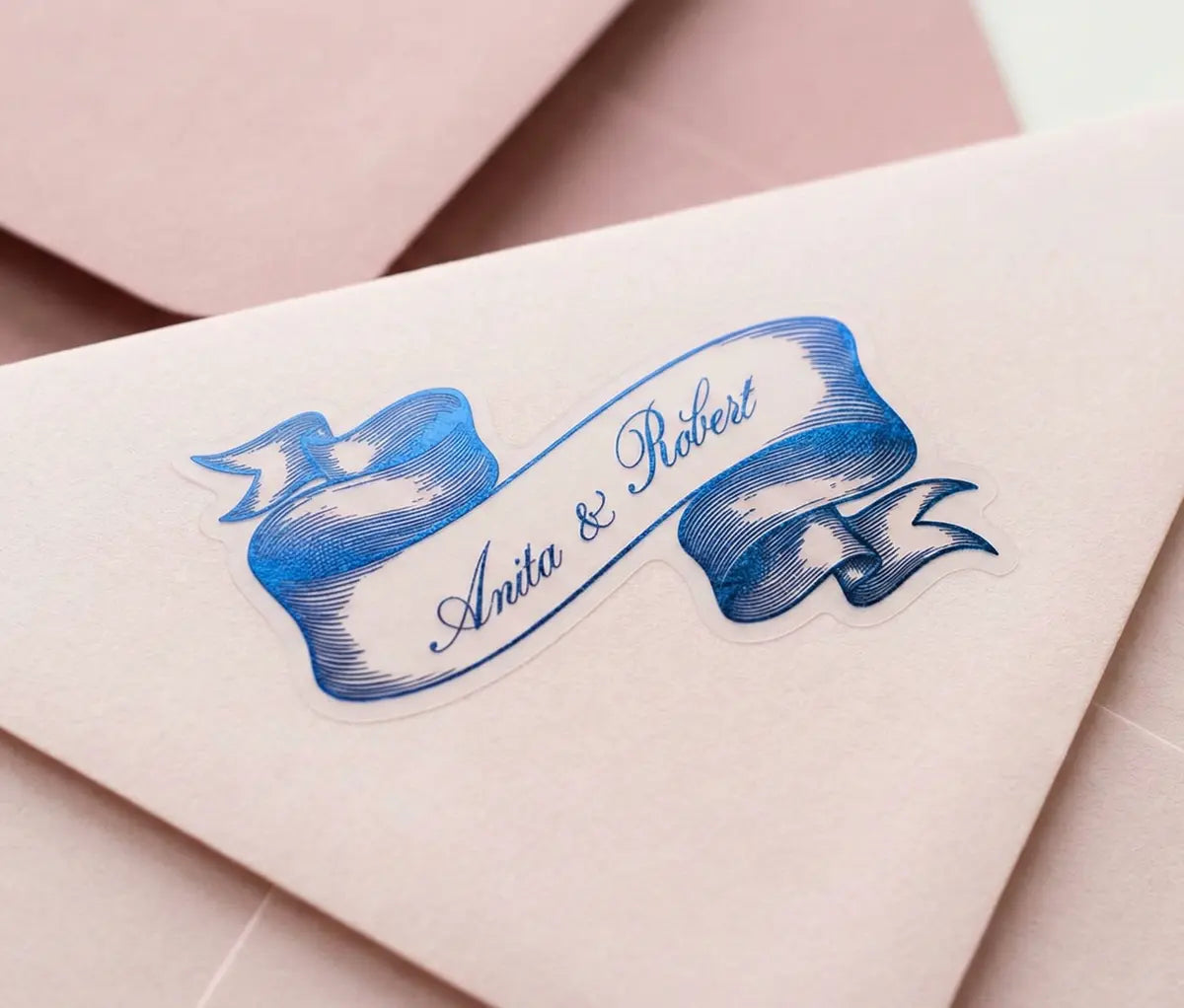Pink Envelope with ribbon-shaped sticker and 'Anita & Robert' text.