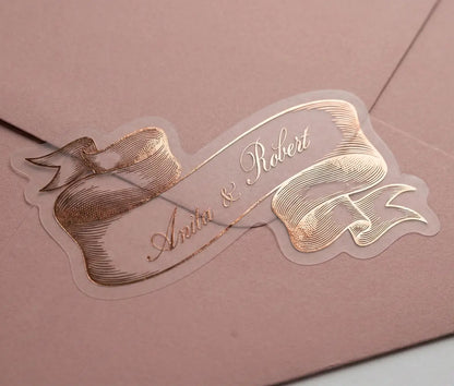 Wedding sticker cut in vintage style ribbon shape with personalized names and rose gold foil print on a pink envelope.