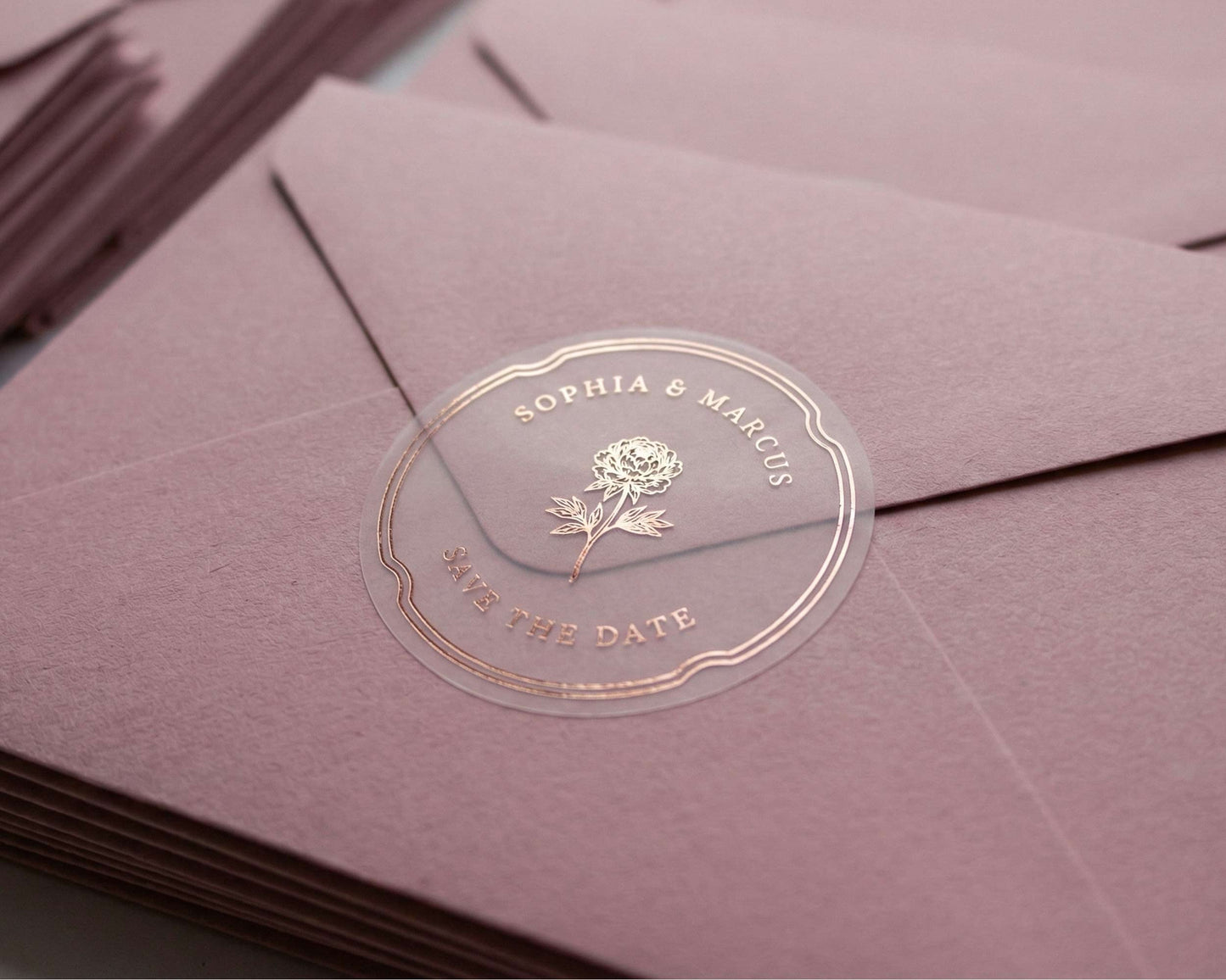 Clear Save the Date sticker with peony graphic and personalized names printed in rose gold foil sealing dusty pink color envelope.