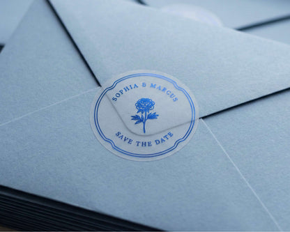 Clear Save the Date sticker with flower graphic and personalized names printed in royal blue foil sealing light blue envelope.