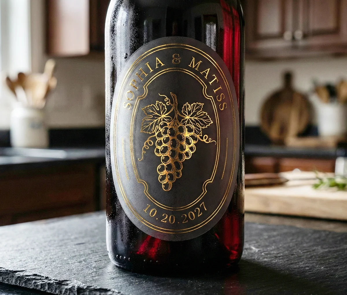 Red wine bottle with an oval personalized frosted label featuring grapes printed in gold foil.