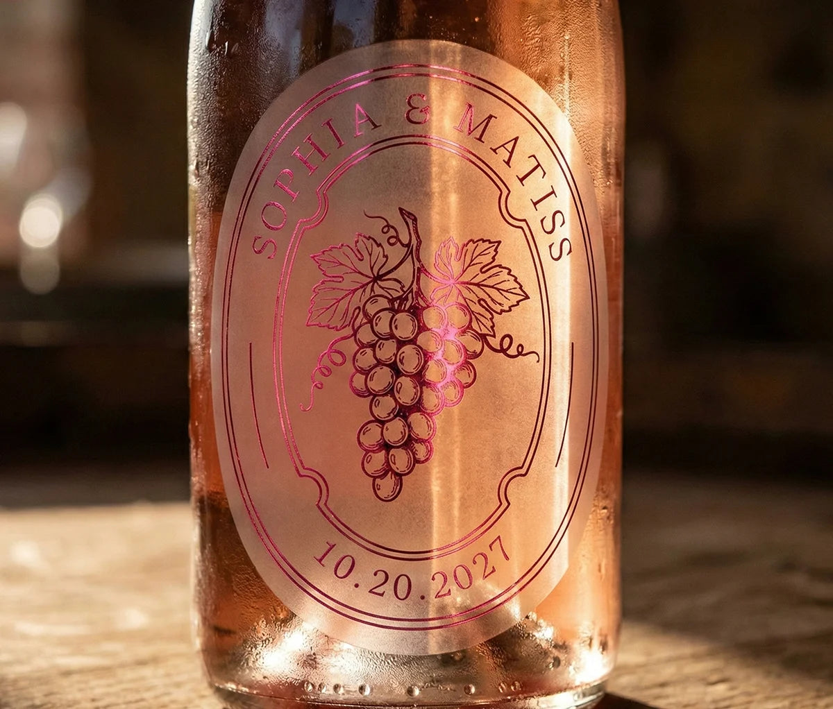Rose wine bottle with an oval personalized frosted label featuring grapes printed in hot pink foil.